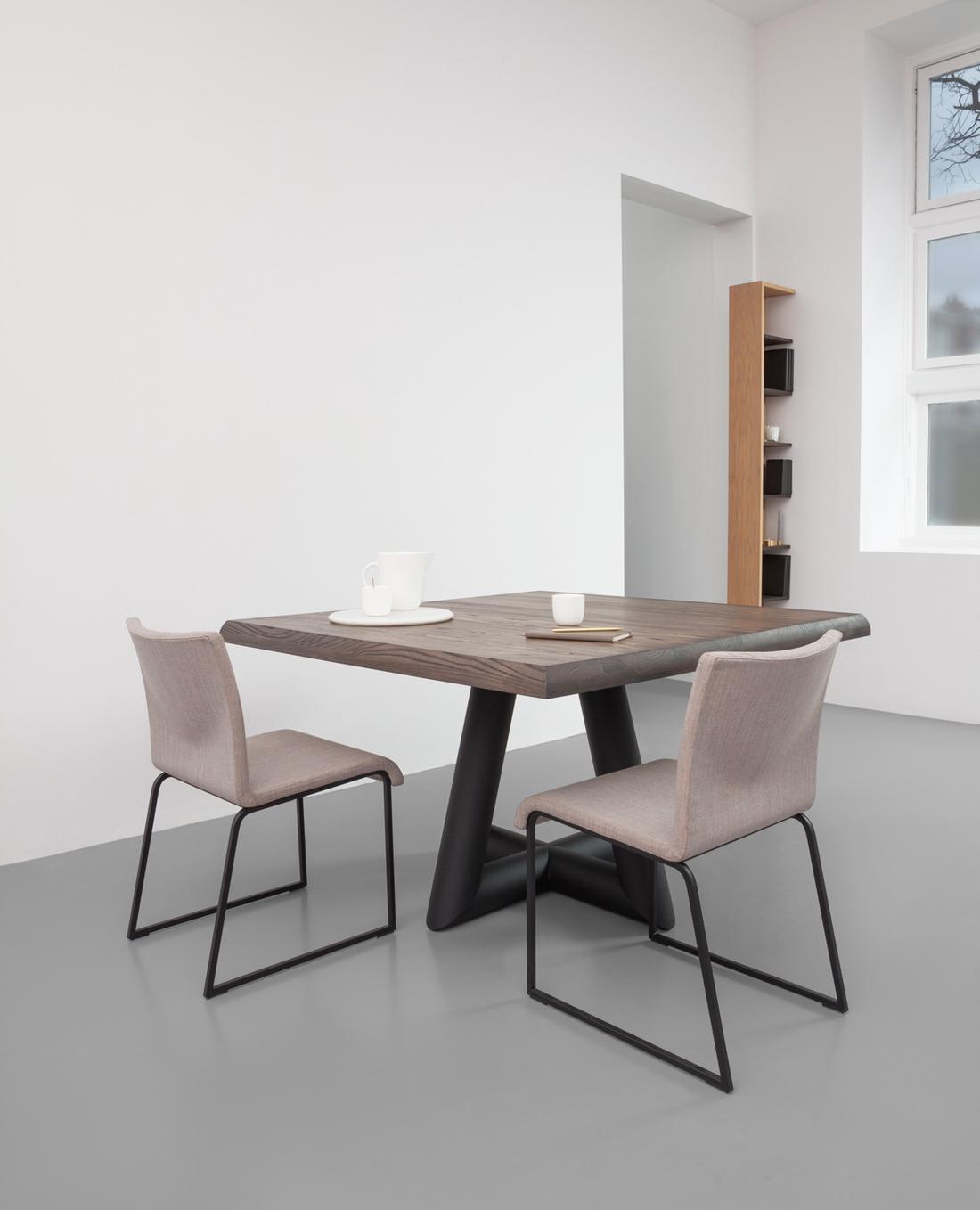 De grote, gepoedercoate stalen buizen onder het tafelblad lijken naar elkaar toe lijken te lopen.