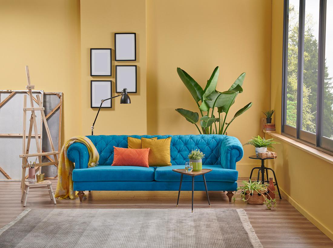 woonhome-kleuren-in-je interieur-gele-muur-blauwe-bank-1